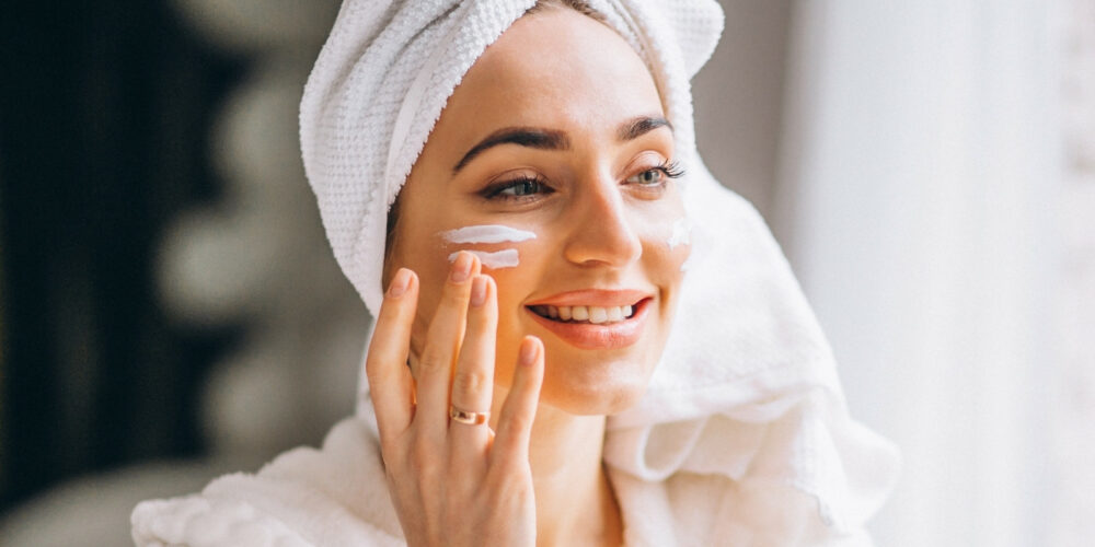 Gesichtscreme anwenden junge frau mit handtuch